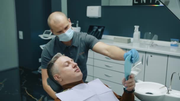 ボールド男性の前向きな歯科医で 中年の灰色の髪の患者が歯をチェックし 鏡を覗き込み 頭を横から横に向けました 高品質の4K映像 — ストック動画