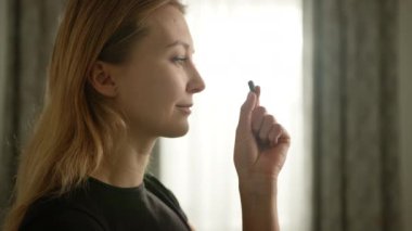 Pencerenin önünde duran genç bir kız, ağzına dikkatlice bir hap koyar ve günlük rutininde sağlığına ve sağlığına bilinçli bir yaklaşımı gösteren bir yudum suyla onu takip eder..