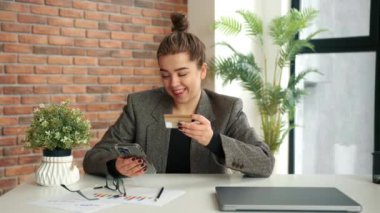 Ofisindeki genç bir iş kadını internetten satın almaktan zevk alıyor. Telefonla kart numarasını giriyor ve online alışveriş yapmaktan mutlu oluyor..