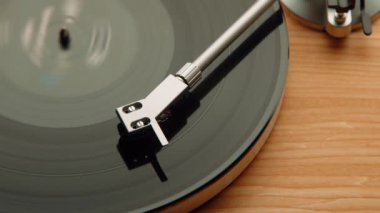  Plakçıların iğnelerini nazikçe albüm yüzeyine değdirirken, dönen diskteki oyuklar, ahşap bir arka plana karşı retro ses teknolojisinin özünü yakalıyor..