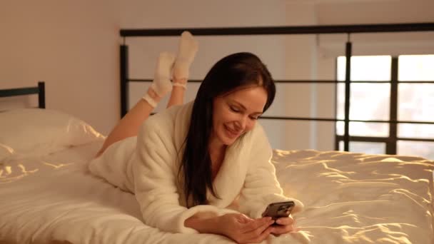 Красивая Женщина Лежит Кровати Телефоном Руках Радостно Кому Пишет Лицо — стоковое видео
