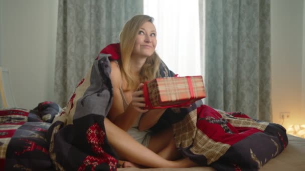Жінка Ліжку Покрита Ковдрою Радісно Розгорнула Подарунок Святковій Коробці Червоною — стокове відео