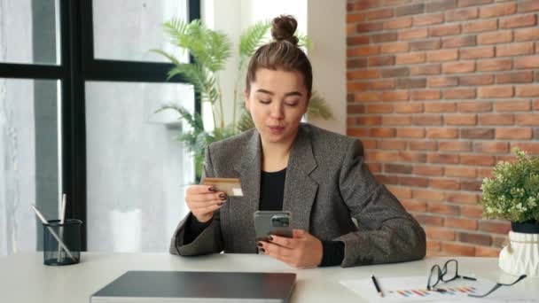 一个在办公室里想用她的智能手机上网购物的女孩 她坐在一间窗户很大的现代化办公室里 输入了她的信用卡号码 红色V Raptor — 图库视频影像