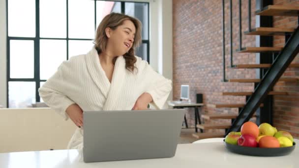 一位身穿白色长袍的年轻女子在明亮的厨房里 一边在笔记本电脑上享受着生动的视频聊天 一边还带着一个生机勃勃的水果碗 给整个场景增添了色彩 — 图库视频影像