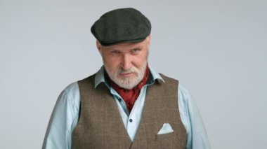 Kırmızı eşarplı orta yaşlı bir adam kameraya kendinden emin bir şekilde başını sallıyor. Jesti onaylama ve güvence göstergesi. Onun şık kıyafeti sofistike portreye ekleniyor. Kırmızı 8K RAW.