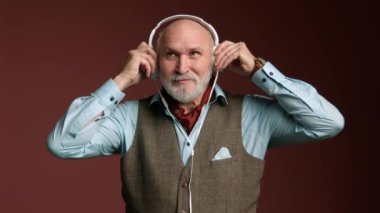Gözlüklü şık bir son sınıf öğrencisi ve hafif gömlekli bir yelek, beyaz kulaklık takıp müzik dinliyor. Adam kel, gri sakallı, yaşını vurgulayan biri. Kırmızı 8K RAW
