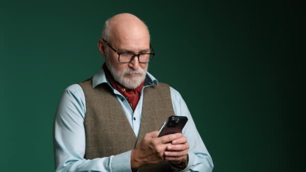 一个年长的男人 在他的智能手机上输入一个消息 他穿着一件背心 一件宽松的衬衫 脖子上戴着一条红围巾 这个人秃头 留着灰白的胡子 时髦的眼镜 红色8K红色 — 图库视频影像