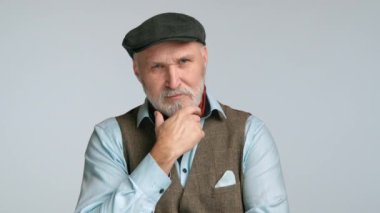 Siyah bir Trilby takarken sakalına dokunan 50 'li yaşlarındaki düşünceli bir adam, düşünceli ve zeki bir görünüm sergiliyor. Onun tüvit yelekli ve mavi gömleği onun tefekküre dayalı davranışını tamamlıyor. 8K HAM.