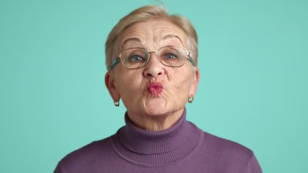 快乐而兴奋的女性养老金领取者 深深的皱纹 浅色的紫色套头毛衣 站在工作室蓝色背景之上 高质量的4K镜头 — 图库视频影像