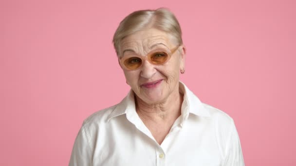 活泼的老太太 留着短发 玩的很开心 在演播室里把脸贴在粉红的背景上 有趣的积极的奶奶 优质4K脚注E — 图库视频影像