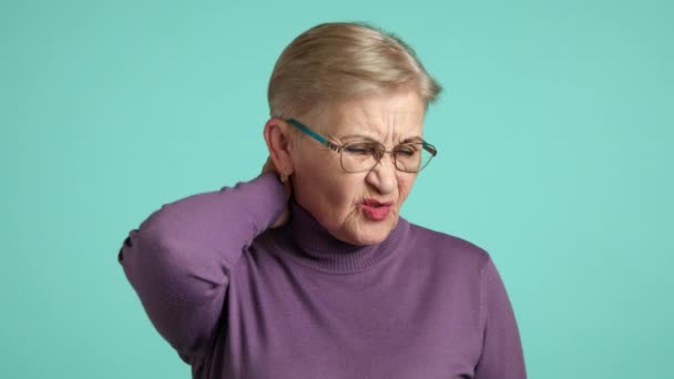 穿着紫色高领毛衣 化着淡妆的老妇人因蓝色背景而痛苦不堪 与年龄有关的健康问题 老年妇女颈部疼痛 高质量的4K镜头 — 图库视频影像