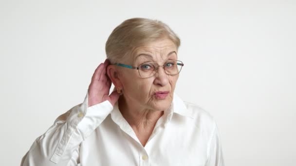 老太太皱纹很深 妆容轻盈 身穿白衬衫 站在白色背景之上 听力有问题 与年龄有关的听力丧失 高质量的4K镜头 — 图库视频影像