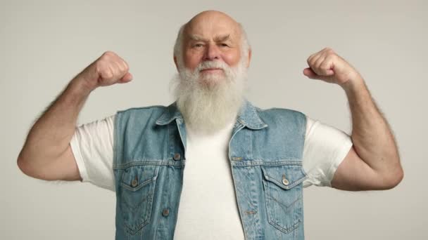 大きなひげを持つハンサムな祖父は 彼の二頭葉を披露する 彼はとても嬉しくて幸せで デニムベストを着ています その背景は白 レッド Raw — ストック動画