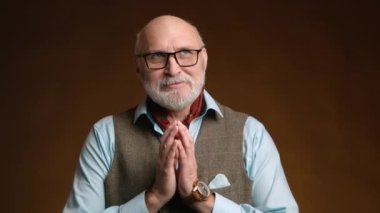 Sağlam bir orta yaşlı adam bir şeyler planlıyor gibi görünüyor. Etrafa düşünceli bir şekilde bakıyor. O, siyah gözlük, klasik bir saat ve kahverengi arka planda bir yelek ile bir gömlek giyiyor. 8K HAM.