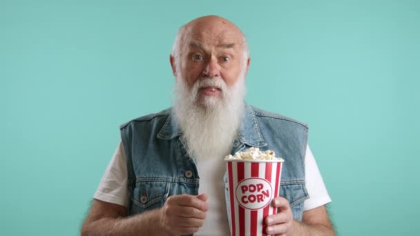 ポップコーンで映画を見ていると楽しいおじいちゃん 彼はスクリーンで見たものに感情的に反応する 男は青いデニムのベストを着た白いTシャツを着ている レッド Raw — ストック動画