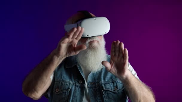 一个留着胡子的老人在虚拟世界里享受着游戏 他戴着Vr眼镜 在虚拟环境中积极观察并与双手互动 — 图库视频影像
