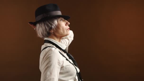 时尚的老年女性 有着时髦的银发 戴着精致的黑色帽子 沉稳地凝视着生活 优雅的轮廓在温暖的背景下显得更加突出 8K照相机 — 图库视频影像