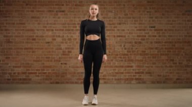 Yan hamleler. Bir antrenör ustalıkla egzersizin nasıl yapıldığını gösterir, yan hamleler. Fiziksel olarak iyi durumda bir kız. Siyah spor kıyafetleri içinde, çatı katında duvarları olan bir spor salonunda. Kamera 8K HAM.