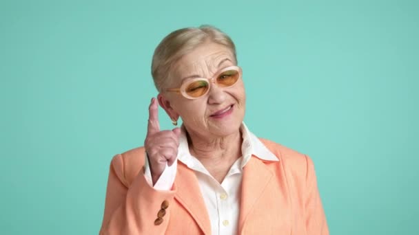 70歳の面白い女性のミディアムショット 白いシャツの短い髪 オレンジのジャケットの笑顔 スタジオのアクアマリン背景の上に立っています 高品質の4K映像 — ストック動画