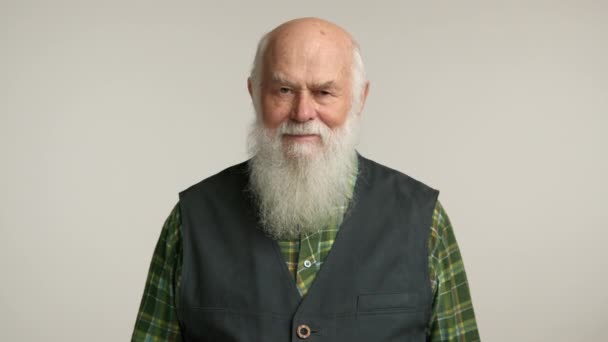 年长的男人 留着长长的白胡子 满面春风 穿着黑色背心 穿着格子呢衬衫 站在中立的背景下 散发着温暖 智慧和沉着的感觉 8K照相机 — 图库视频影像