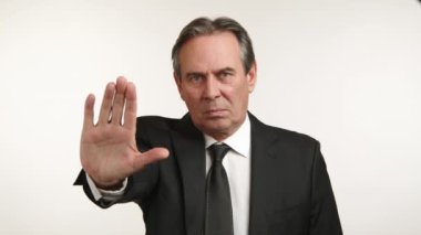 Koyu takım elbiseli iddialı bir işadamı beyaz bir zeminde kesin sınırlar koyduğunun açık bir işareti olan dur hareketi yapar. Kamera 8K HAM. 