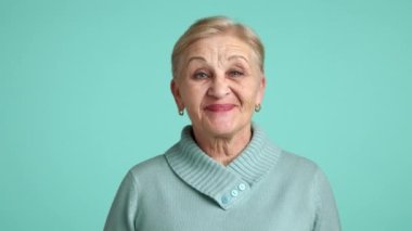 60-70 yaşlarında, kısa sarı saçlı mavi süveter giyen, mavi arka planda duran, birini destekleyen, biriyle aynı fikirde olan düzenli bir kadın. Yüksek kalite 4k görüntü