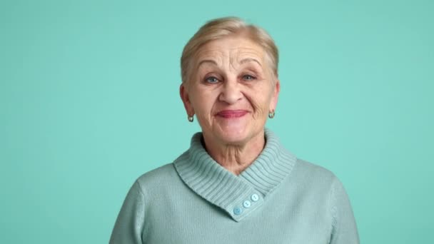 一位60岁至70岁的漂亮女士 一头金发短发 穿着蓝色毛衣 站在蓝色背景之上支持某人 与某人意见一致 高质量的4K镜头 — 图库视频影像