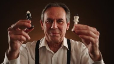 Neşeli bir adam bir kral ve kraliçe satranç taşını tutuyor, gülüyor ve satranç oynamaktan zevk alıyor, meydan okuma ve stratejiye olan aşkını gösteriyor. Yüksek kalite 4k görüntü