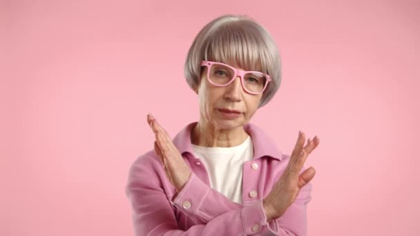 持怀疑态度的老妇人 戴着粉色眼镜 在柔和的粉色背景下摆出一副毫无表情的样子 表示不同意 — 图库视频影像