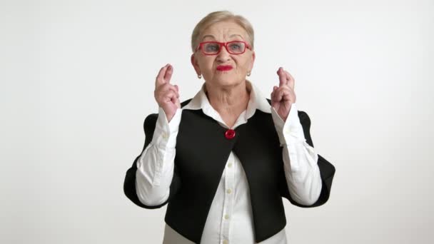彼女の指を横切る赤いメガネを持つ楽観的な高齢女性 白い背景に対する肯定的なニュースを望む — ストック動画