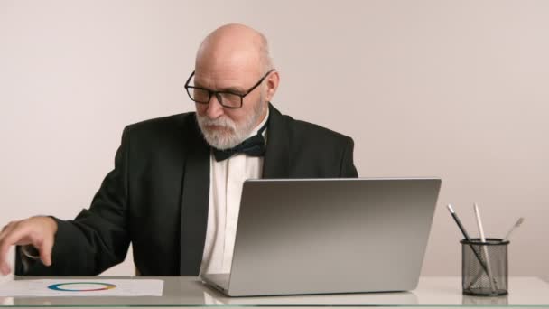 一位穿着正式燕尾服的资深商人仔细地阅读文件 面前打开了笔记本电脑 象征着对他工作的热诚 8K照相机 — 图库视频影像