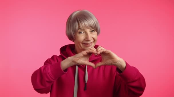 Warm Hearted Senior Lady Pink Hoodie Smilingly Creates Heart Shape — Stock Video