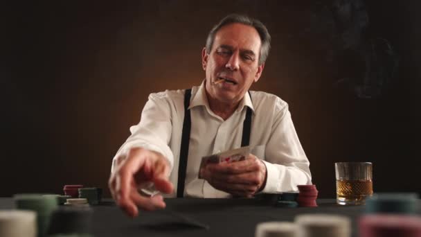 ポーカーゲームに深く魅了された高齢男性は 自信を持って口にリットルタバコとウイスキーグラスを手元に置き 陰の部屋に置きました カメラ Raw — ストック動画