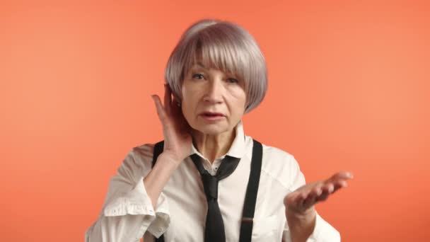 灰色の髪の成熟した女性は 耳に手を押し オレンジ色の背景に耳を傾けようとします カメラ Raw — ストック動画