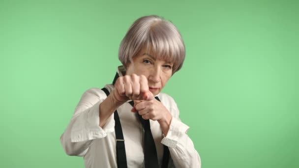 一位坚定的老年妇女准备好了拳头 展示了她的自卫姿态 描绘了绿色背景下的力量和赋权 8K照相机 — 图库视频影像