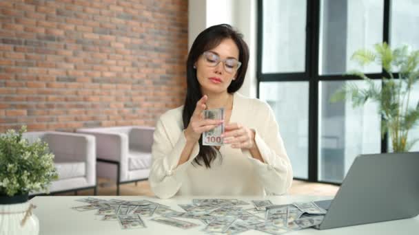 女性は 金に囲まれた現代の机に座っている間 物質的な富に対する彼女の無関心を象徴する100ドルの法案を無条件に涙します カメラ Raw — ストック動画