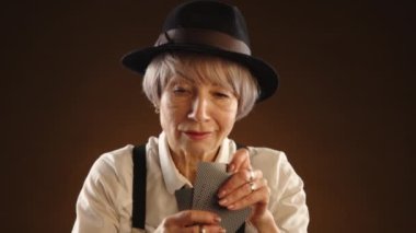 Siyah şapkalı ve pantolon askısı takmış dalgın yaşlı bir bayan, klasik bir oyun atmosferini çağrıştıran sıcak, loş bir ortam olan kart oyununa odaklanır. Kamera 8K HAM. 