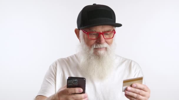 一位戴黑帽 戴着红色眼镜的老年绅士正在使用智能手机和信用卡上网购物 这凸显了数字交易的便利性 8K照相机 — 图库视频影像