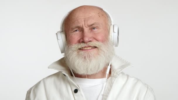수염을 기뻐하는 노인은 음악에서 오버이어 헤드폰을 착용하고 깨끗한 배경에 시간을 — 비디오