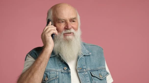 완전한 수염을 남자는 전화에 대화를하고있다 조끼를 부드러운 분홍색 배경에 대하여 — 비디오