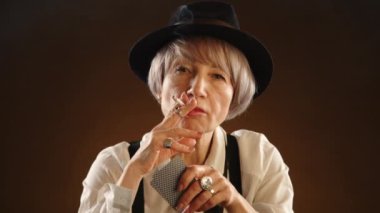 Anlayışlı yaşlı bir bayan bir sonraki hamlesini poker oyununda düşünür, elinde yanan bir puro, odaklanmış bir arka planda. Kamera 8K HAM.