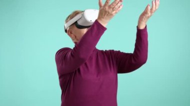 Burgundy balıkçı yaka kazaklı, düzgün, yaşlı bir kadın sanal gerçeklik kulaklığını test ediyor, uzayda el sıkışıyor, oyunlar oynuyor, sanal gerçeklikle etkileşimde bulunuyor. Yüksek kalite 4k görüntü