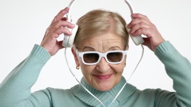 Die Fröhliche Blonde Seniorin Mit Weißrandiger Brille Und Weißen Kopfhörern — Stockvideo