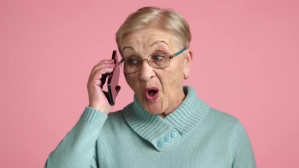 60岁至70岁 身披眼镜 身材苗条 身材苗条 身材苗条 身材苗条的金发女性 穿着蓝色毛衣 手持手机 站在粉色背景下 不期而遇的电话 — 图库视频影像