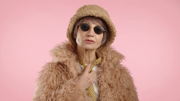 在六十多岁的时候 一位穿着毛皮大衣 头戴水桶帽的时髦女人笑了 她的口音是黄色圆点领带和粉色背景的时髦黑色太阳镜 8K照相机 — 图库视频影像