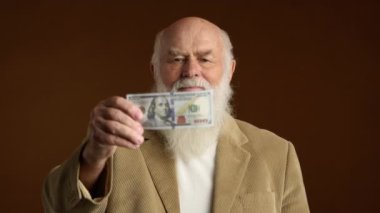 Bej takım elbiseli kıdemli bir adam, kahverengi arka planda yüz dolarlık banknotu yırtarken inanmadığını ya da hayal kırıklığına uğradığını ifade ediyor. Kamera 8K HAM. 