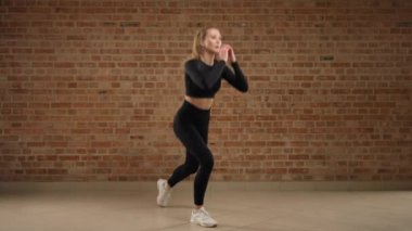Alternatif ters hamleler. Bir antrenör ustalıkla egzersizin nasıl yapılacağını gösterir, alternatif ters hamleler. Fiziksel olarak iyi durumda bir kız. Çatı katındaki bir spor salonunda siyah spor giydi. 8K HAM.