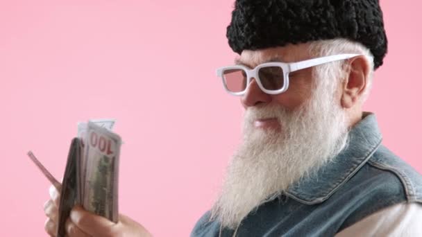 金持ちの老紳士は コンテンツ笑顔 スポーツ白いサングラス パステルピンクの背景に設定したお金を数えています カメラ Raw — ストック動画
