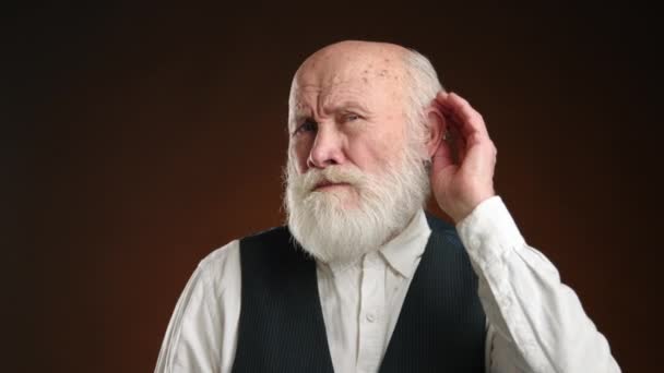 一个满头白胡子的多愁善感的老年男子立刻被抓住 调整他的耳朵 唤起他的好奇心或倾听 面对着身着正式服装的浓郁的深色背景 8K照相机 — 图库视频影像