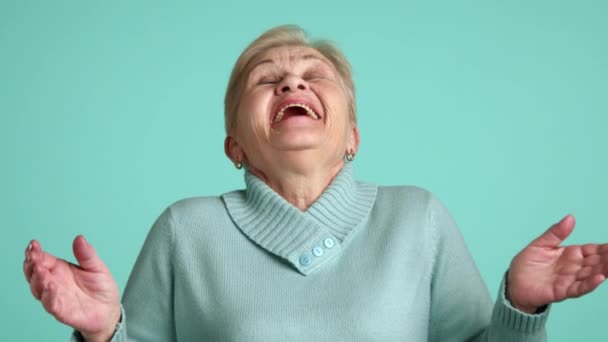 高个子金发女士 穿着蓝色毛衣 头仰起双手 笑着站在蓝色的背景上 幽默的女性养老金领取者 高质量的4K镜头 — 图库视频影像
